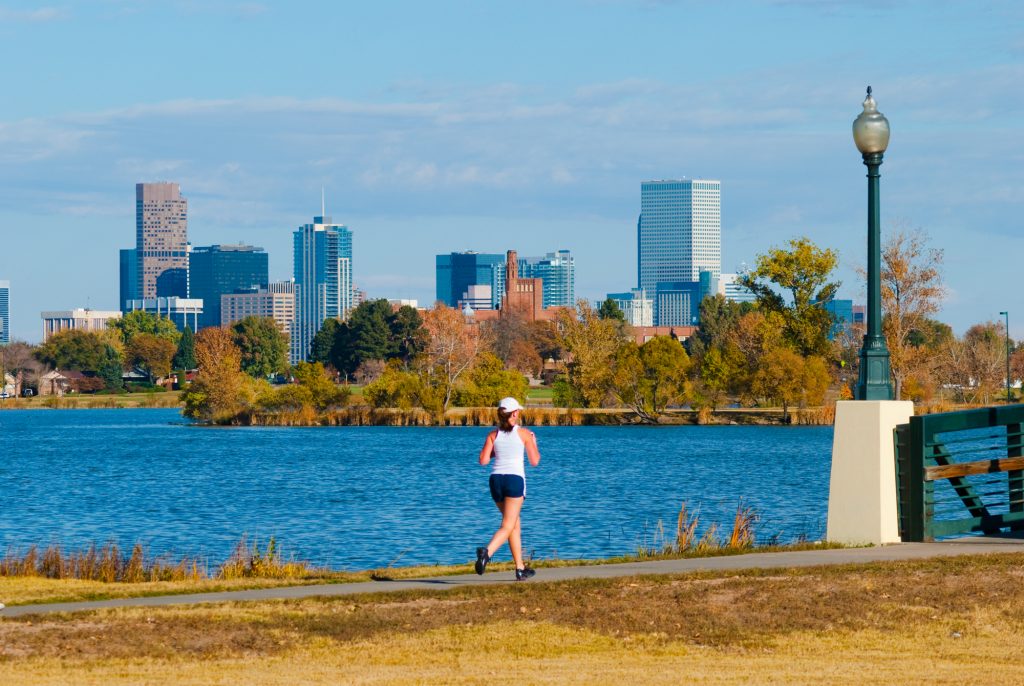 Denver, Colorado, United States - A woman in the foreground jogs near Sloan Lake with the Downtown Denver skyline in the background.