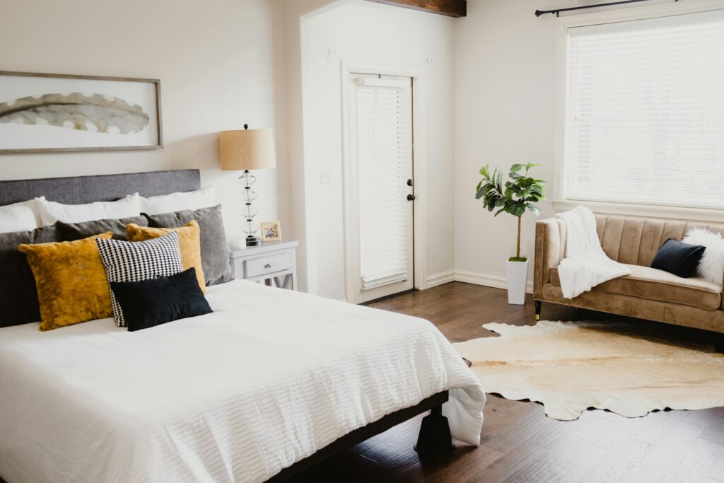 Staged primary bedroom with crisp white bedding, layered pillows and a cozy seating area