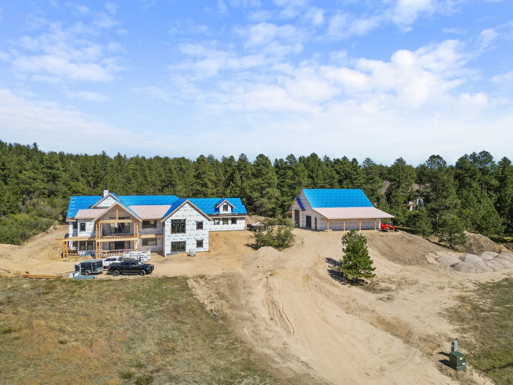 Custom home under construction in a wooded area of Colorado, featuring a large garage and spacious lot surrounded by tall pine trees