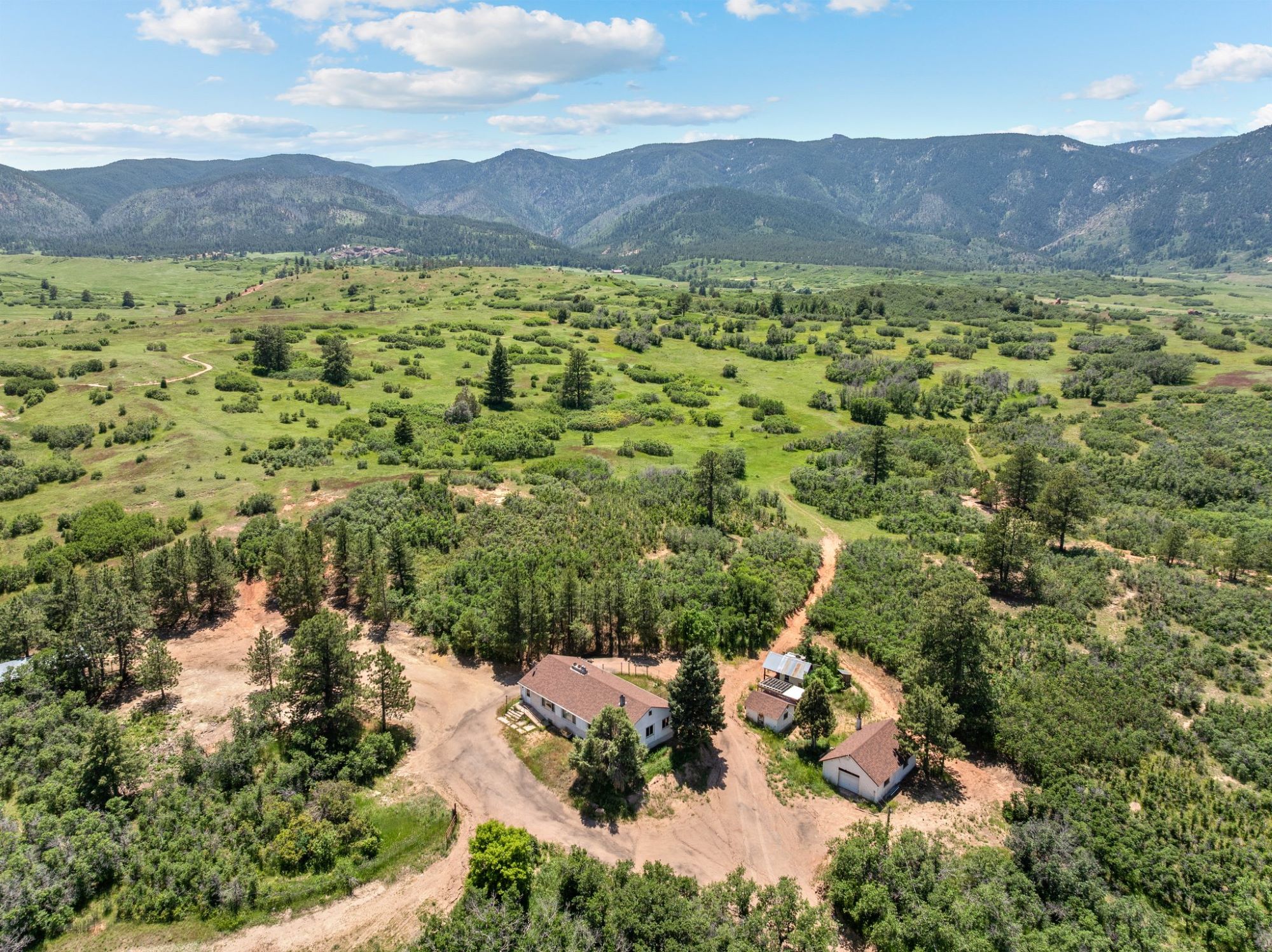 Lush green ranch land in Larkspur, Colorado surrounded by hills and valleys, with buildings nestled in mature trees and meandering dirt roads.