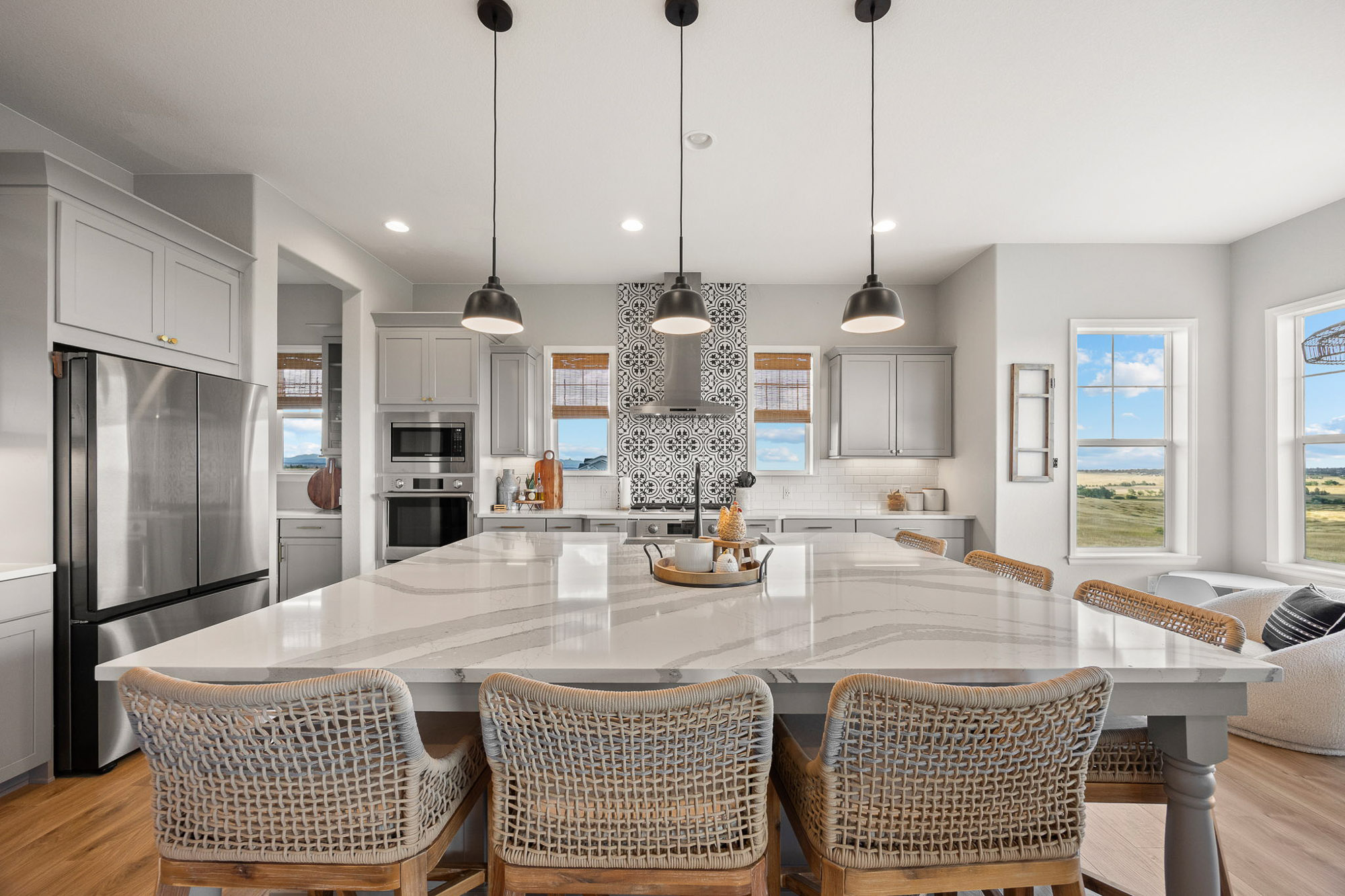 Designer kitchen featuring oversized quartz island, pendant lighting, custom gray cabinetry, and stainless-steel appliances.