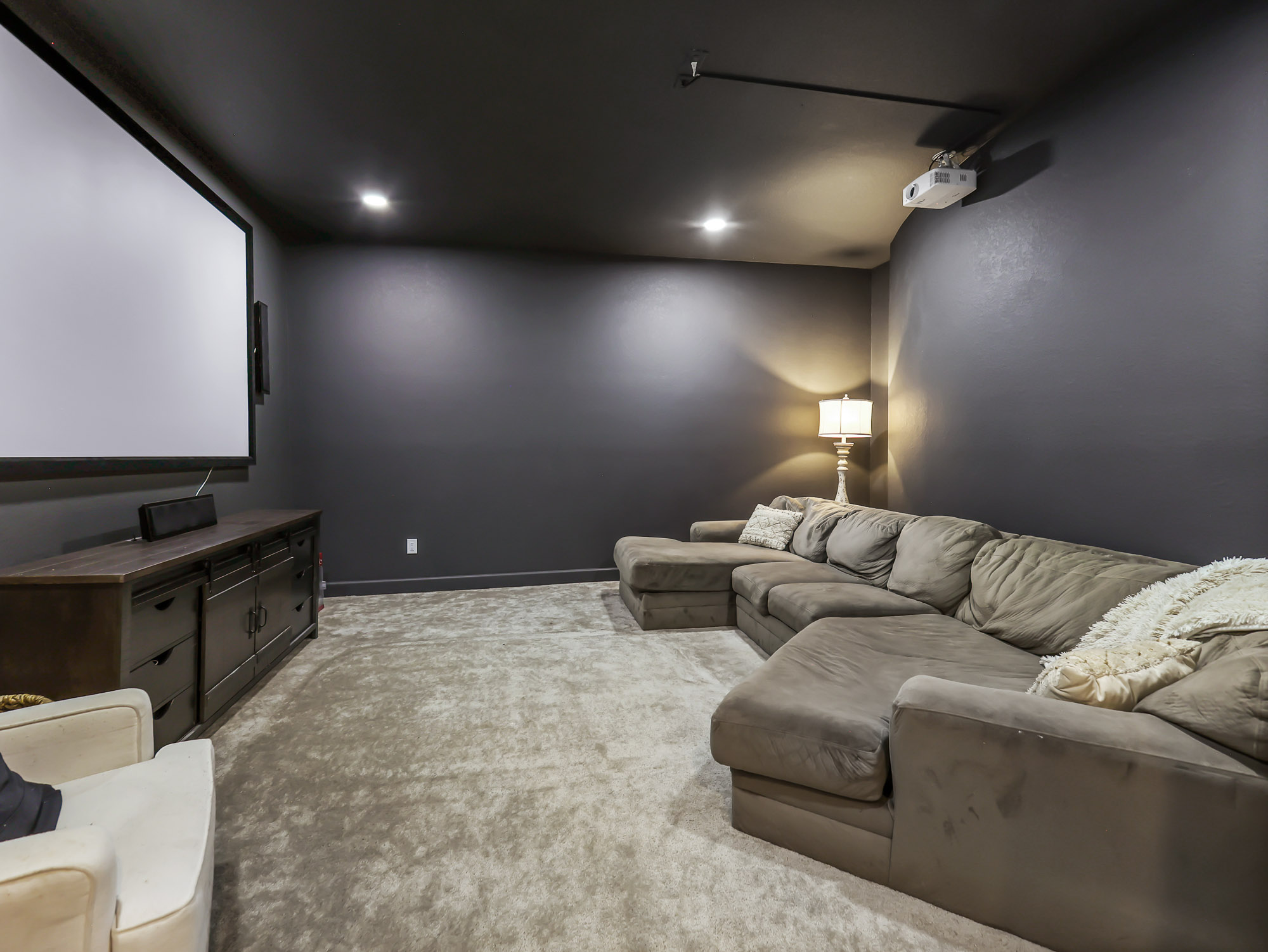 Home theater with large projection screen, sectional sofa, and dark acoustic walls.